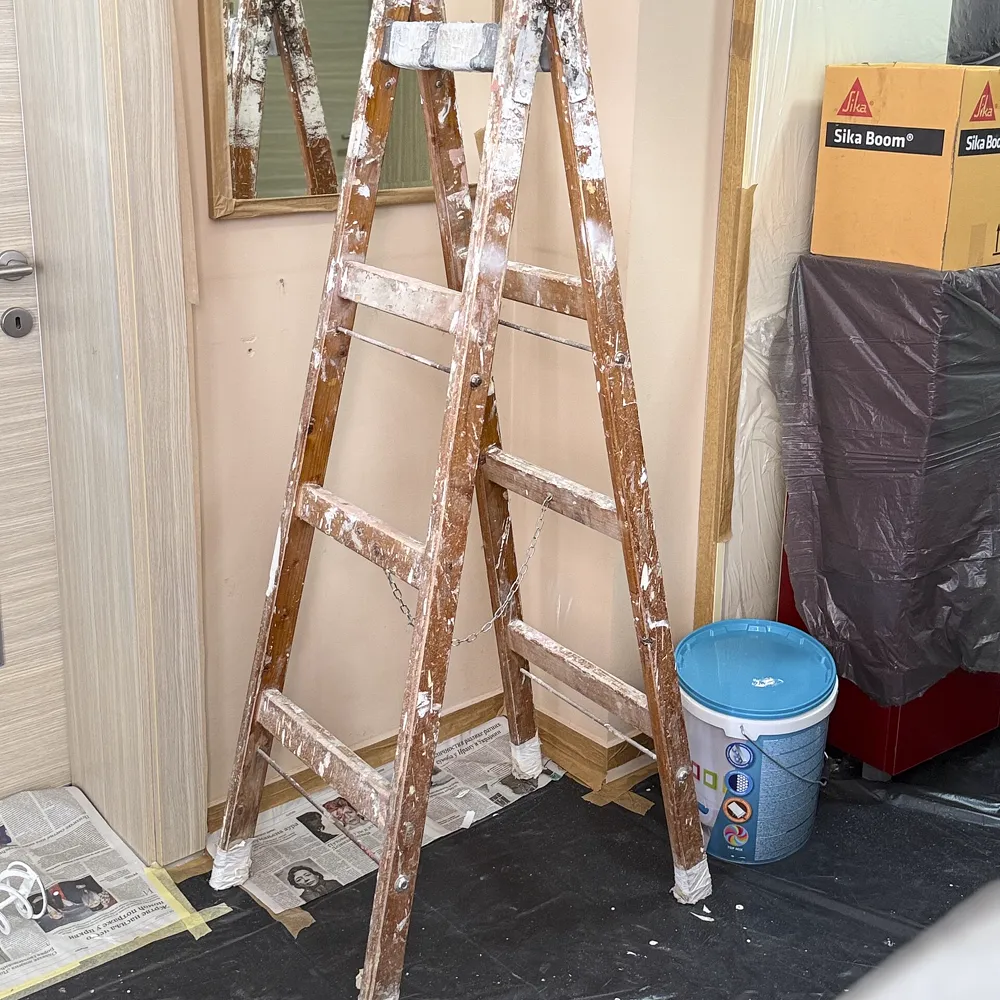 Una scala da imbianchino sporca di pittura appoggiata al muro, teli di nylon e secchi in una stanza in lavorazione